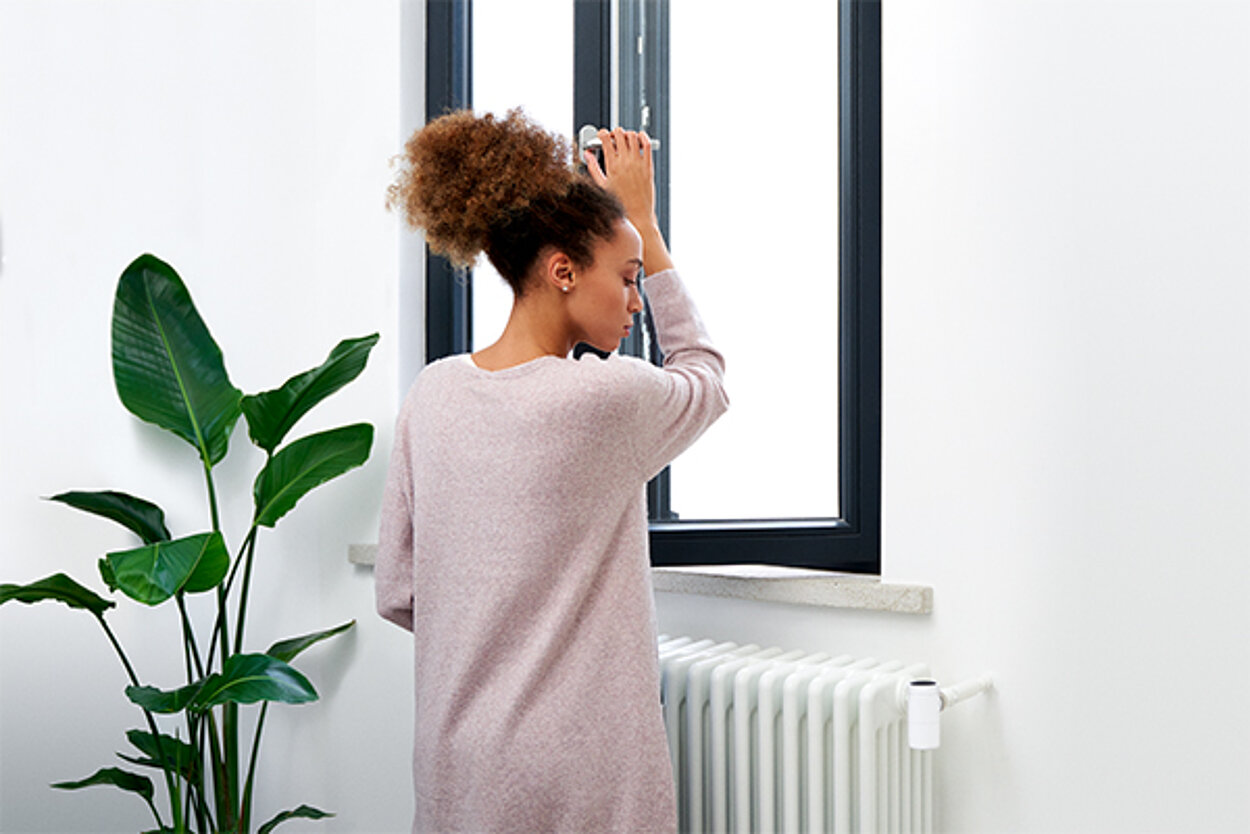 Smartes Thermostat mit Fenster offen Erkennung Junge Frau öffnet ein Fenster und schaut auf den Heizkörper.